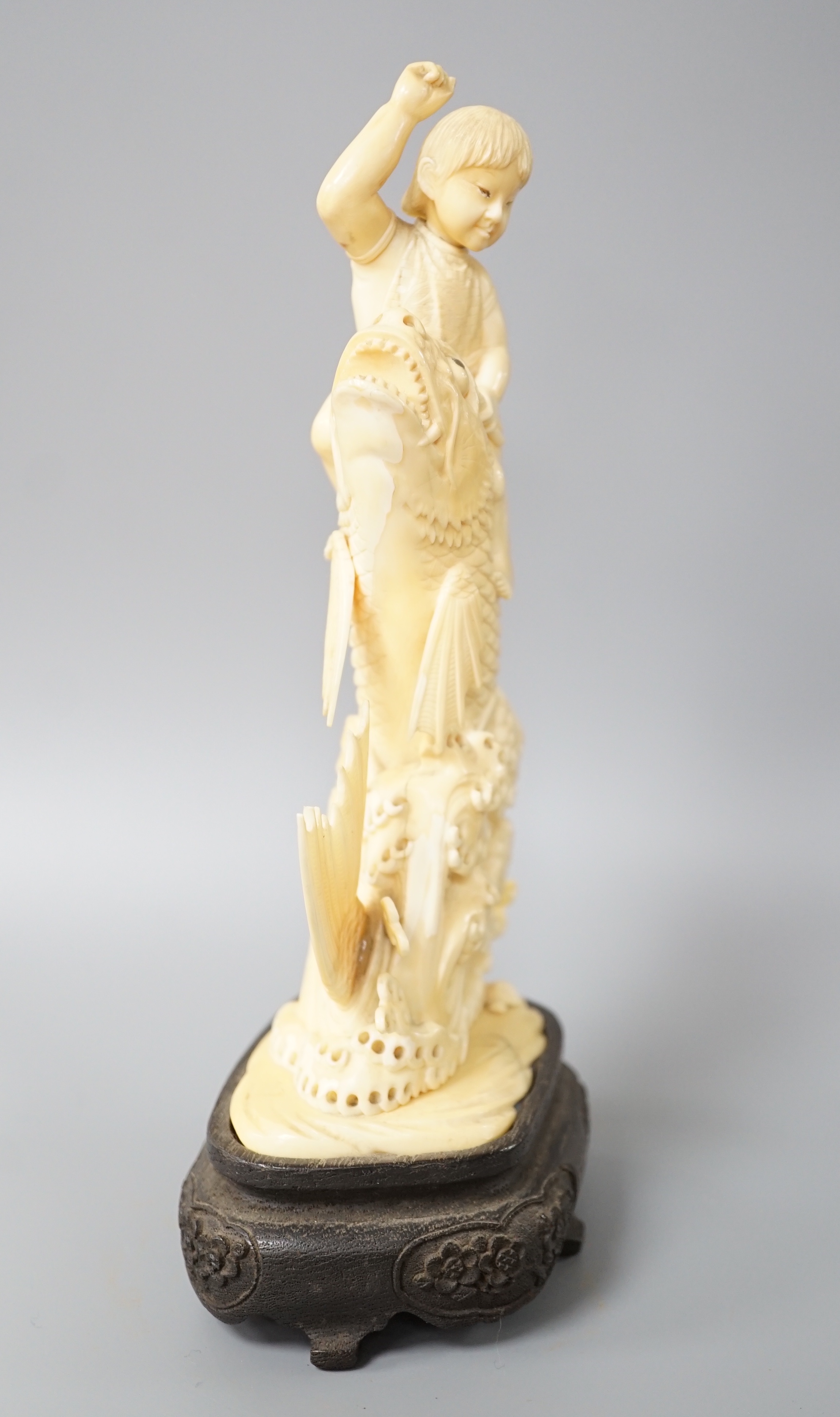 A Japanese sectional ivory okimono of a boy riding a leaping carp, early 20th century, wood stand, 25cm